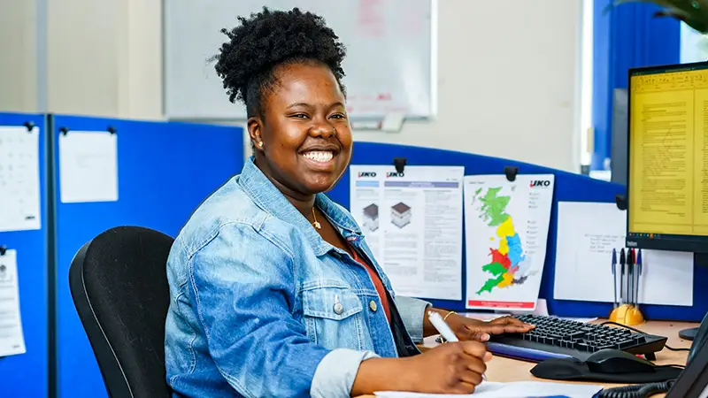 Photo of a member of the IKO Technical Services Team working at her desk and smiling at the camera